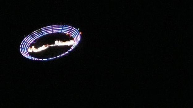 Une soucoupe volante éclairée par des Led et emportée par un hélicoptère